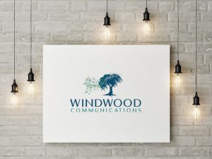 White wall with poster displaying company logo for Windwood Communications framed by hanging lights